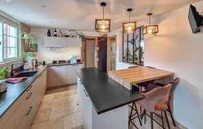A modern kitchen with a central island, bar stools, and pendant lighting. - Belle maison rénovée (Dax)