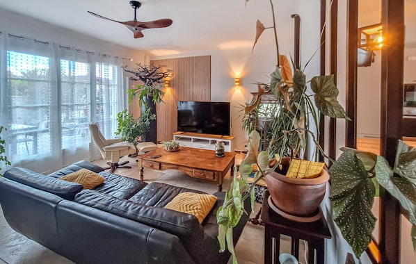 A modern living room with a leather sofa, a wooden coffee table, a TV, and various potted plants. - Belle maison rénovée (Dax)