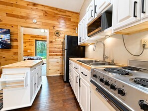 A compact kitchen with wooden walls, a built-in stove, and a refrigerator.