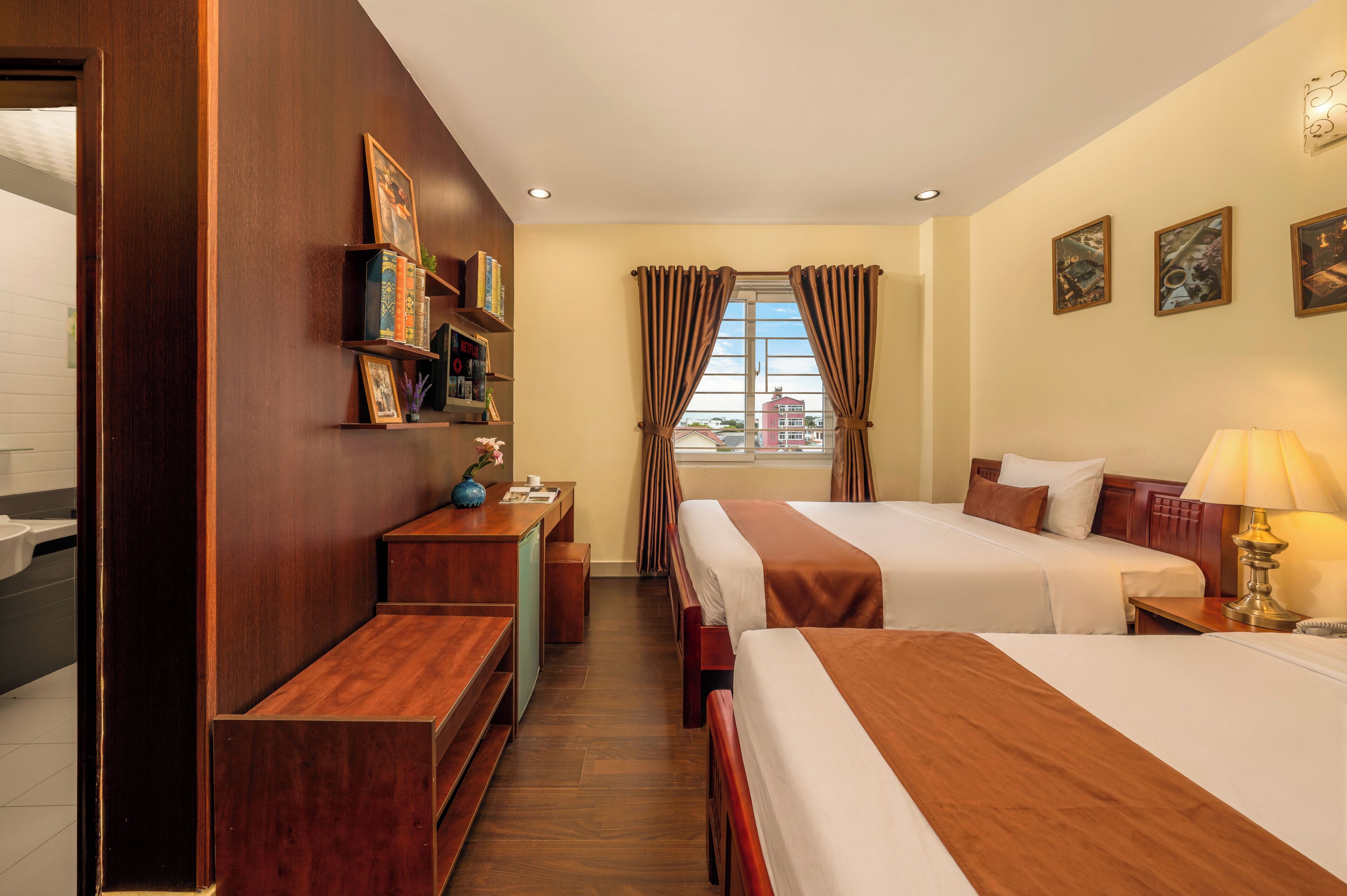 A hotel room with two beds, a desk, a vanity, and a window with curtains.