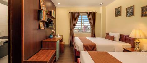 A hotel room with two beds, a desk, a vanity, and a window with curtains.