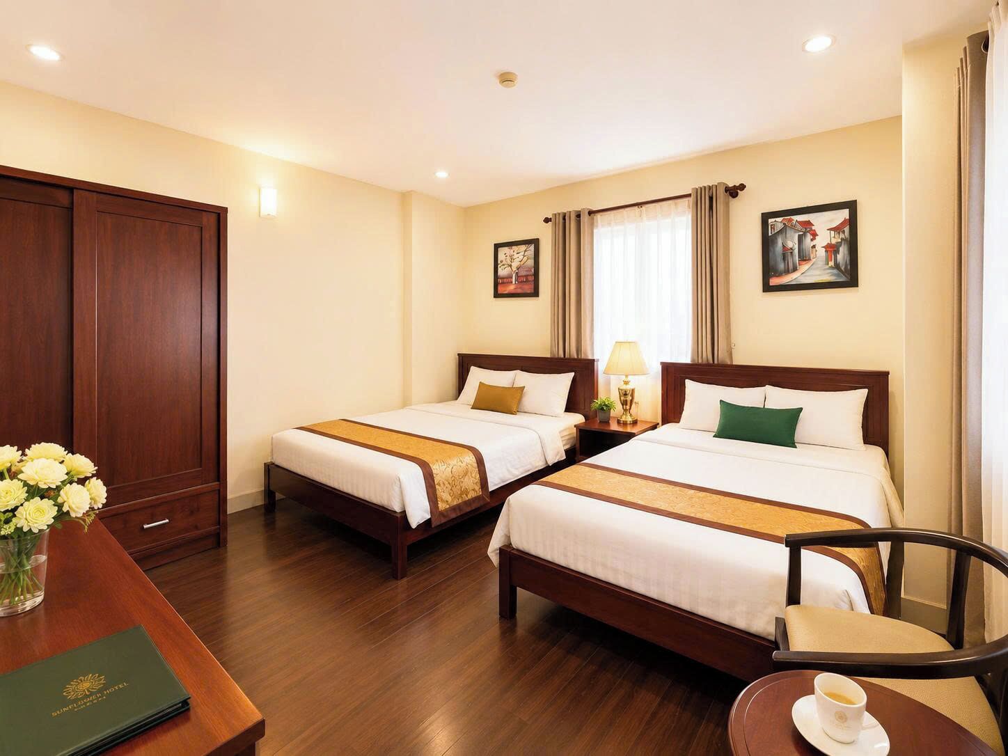Ein Hotelzimmer mit zwei Betten, einem Schreibtisch mit Stuhl, einem Couchtisch, einer Blumenvase und einem gerahmten Bild an der Wand.