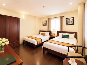 Ein Hotelzimmer mit zwei Betten, einem Schreibtisch mit Stuhl, einem Couchtisch, einer Blumenvase und einem gerahmten Bild an der Wand.