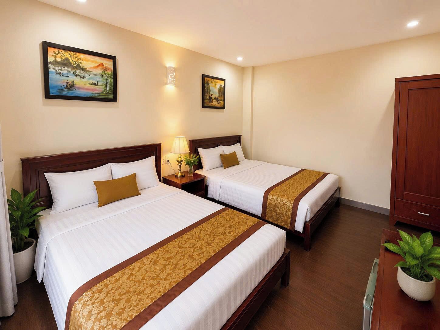 Ein Hotelzimmer mit zwei Betten, einem Nachttisch mit Lampe, einem Kleiderschrank und zwei an der Wand hängenden Bildern.