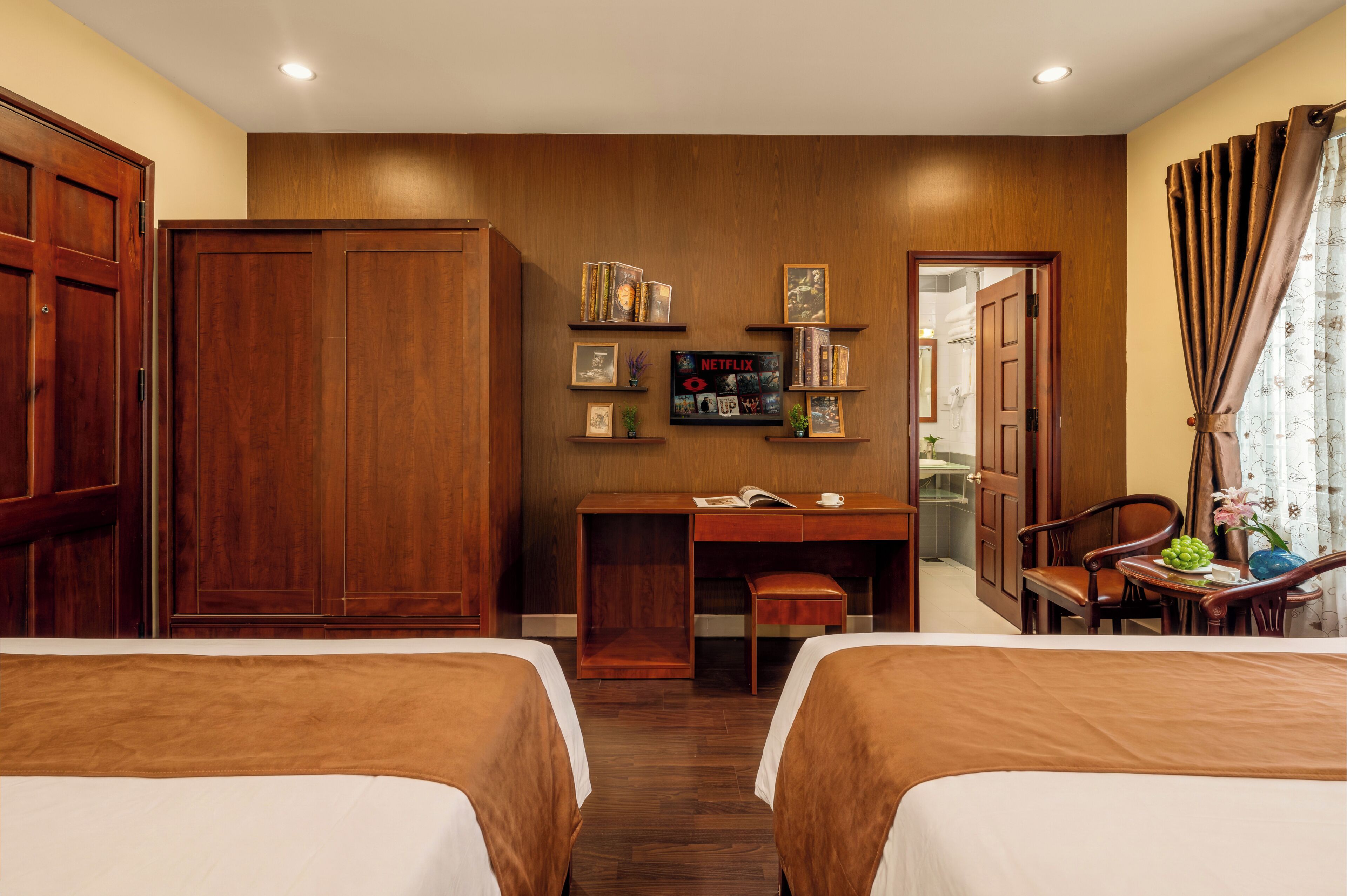 A hotel room with two beds, a desk, a wardrobe, and a small seating area.