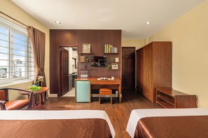 Een hotelkamer met twee bedden, een bureau, een kleine koelkast, een boekenkast en uitzicht op de stad.