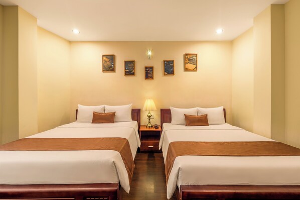 Habitación de hotel con dos camas, una mesita de noche, una lámpara y cuatro cuadros en la pared.
