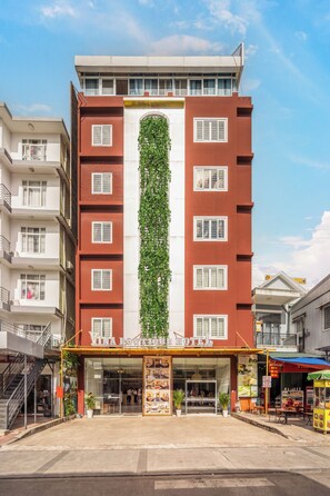 Un hotel con fachada roja, varias ventanas y un jardín vertical verde.