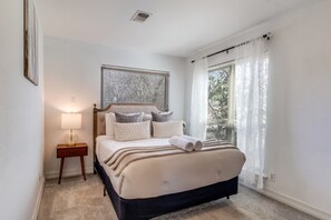 Ein Schlafzimmer mit Bett, Nachttisch, Lampe und Fenster mit Vorhängen.