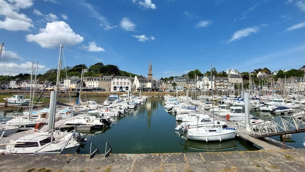 Un port de plaisance où sont amarrés de nombreux bateaux, une tour imposante en arrière-plan et des bâtiments qui bordent la rive.