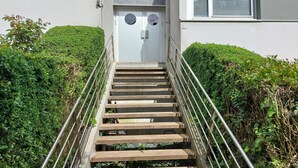 Un escalier en bois, doté de rampes en métal, mène à une porte blanche ornée de fenêtres rondes.