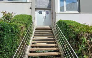 A wooden staircase with metal railings leading to a white door with circular windows. - Studio proche de la mer (Saint-Quay-Portrieux)