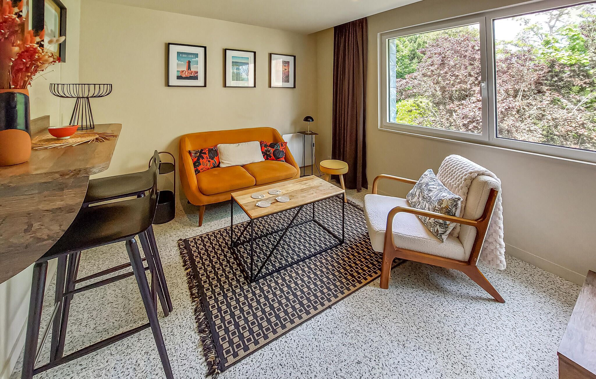 A living room with a sofa, a chair, a coffee table, a rug, and a window with a view of trees.