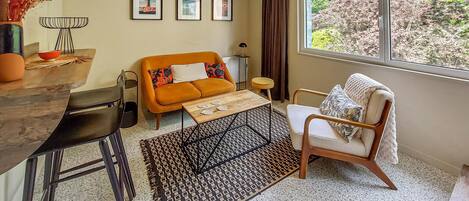 A living room with a sofa, a chair, a coffee table, a rug, and a window with a view of trees.