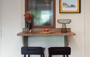 A dining area with a wooden table, two black chairs, a vase with dried flowers, a red bowl, and a framed picture on the wall. - Studio proche de la mer (Saint-Quay-Portrieux)