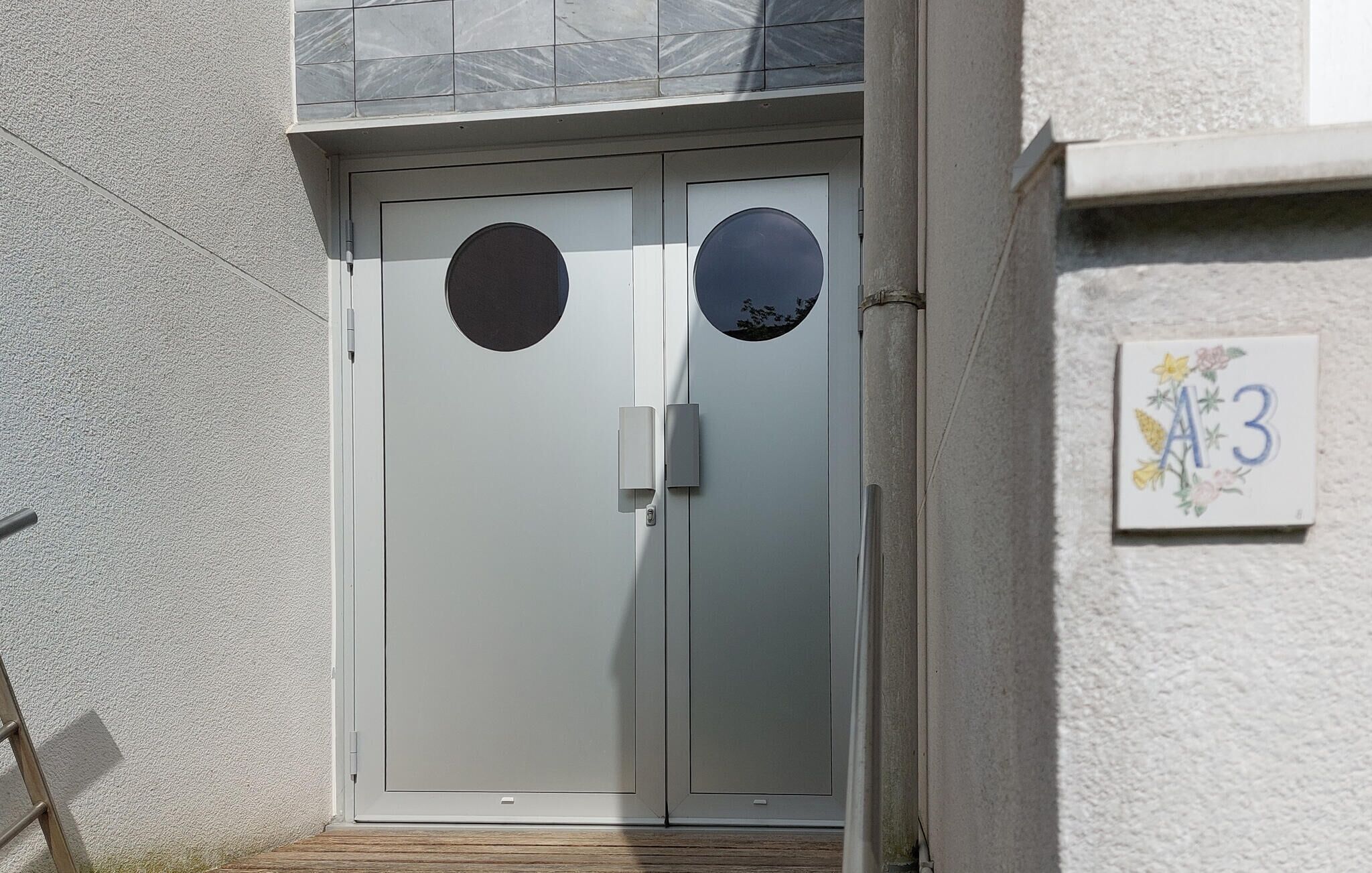 A double door with a circular window on each door, a small light fixture, and a house number plaque.