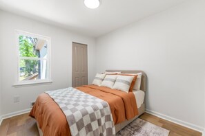 A bedroom with a bed, a window, a door, and a rug.