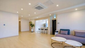 A spacious living area with a sofa, two small tables, a potted plant, and a kitchen in the background. - Ayana Hotel & Resort (Mokpo)