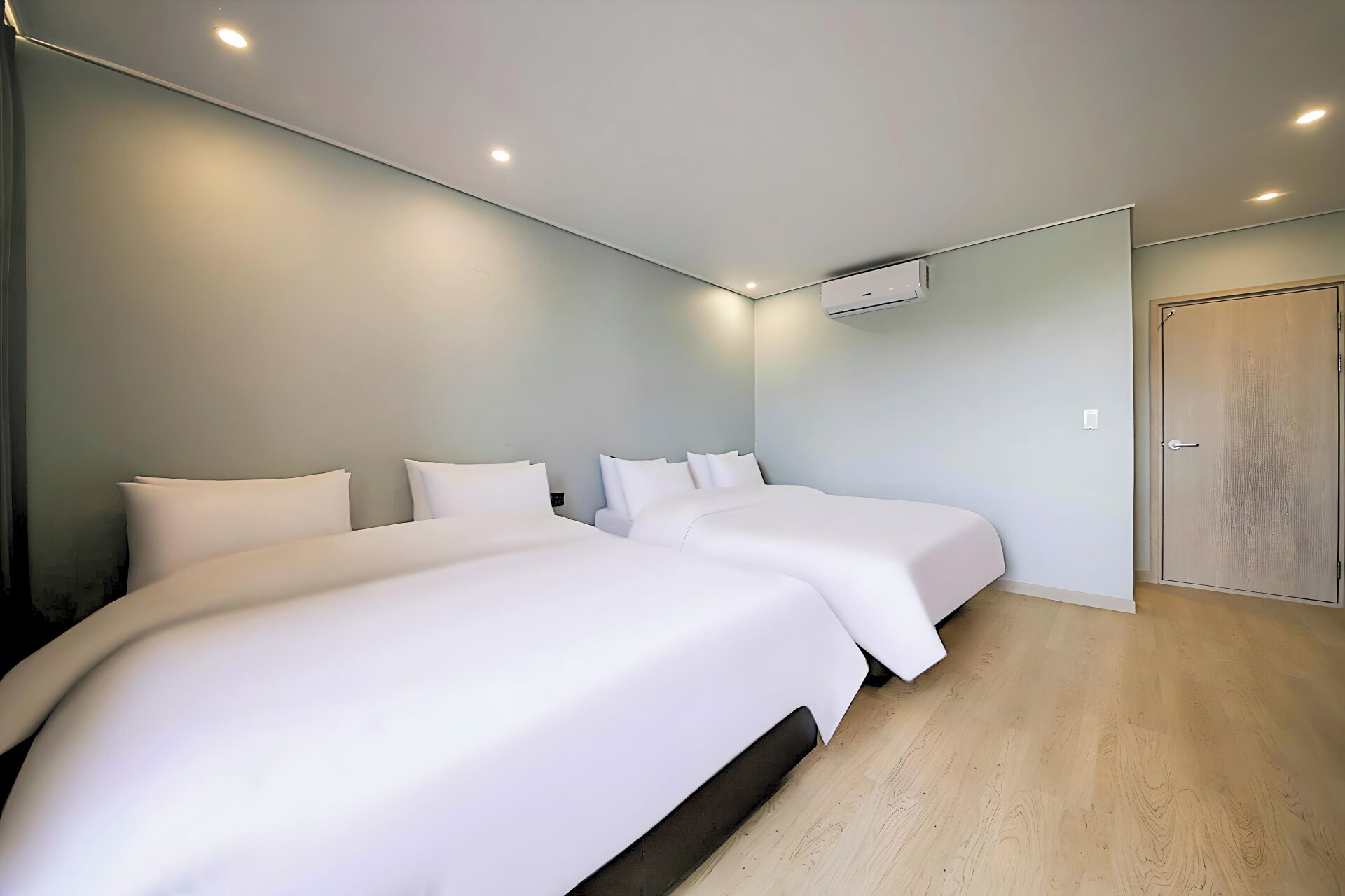 A modern hotel room with two beds, a wooden floor, and a door.