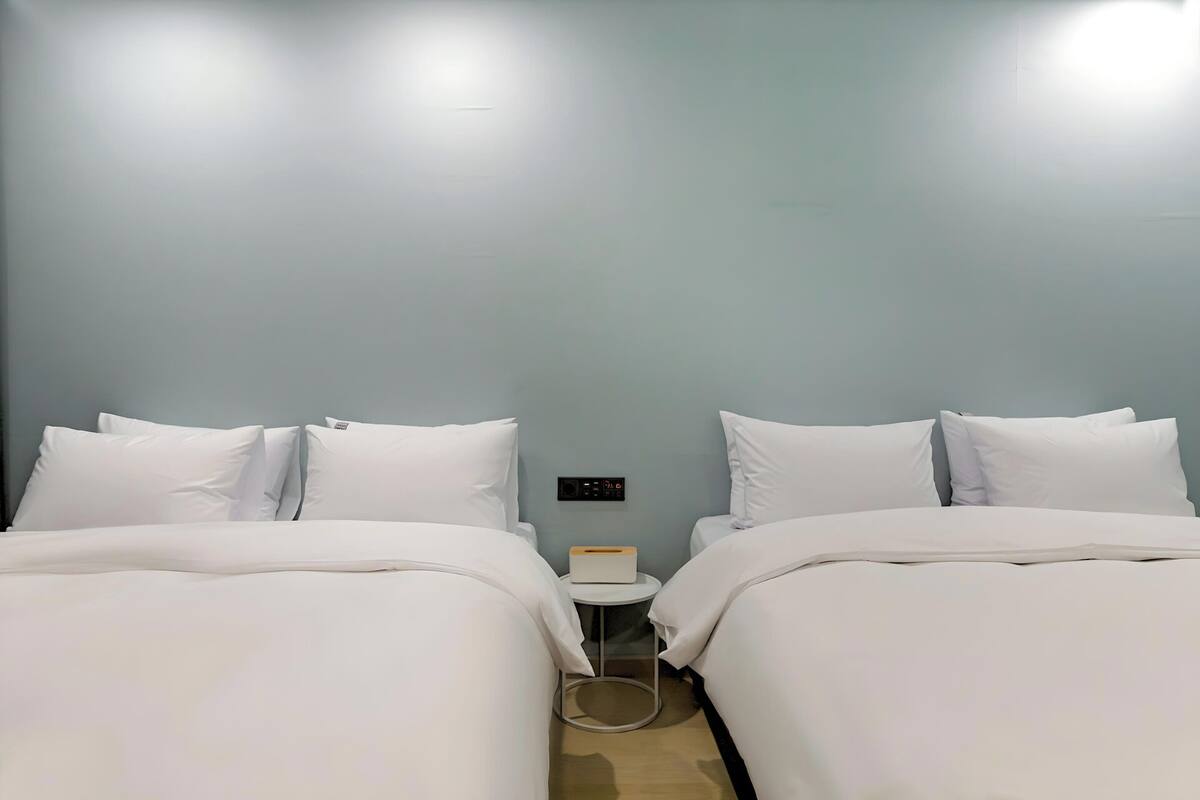 A hotel room with two beds, a small bedside table, and a wall-mounted control panel.