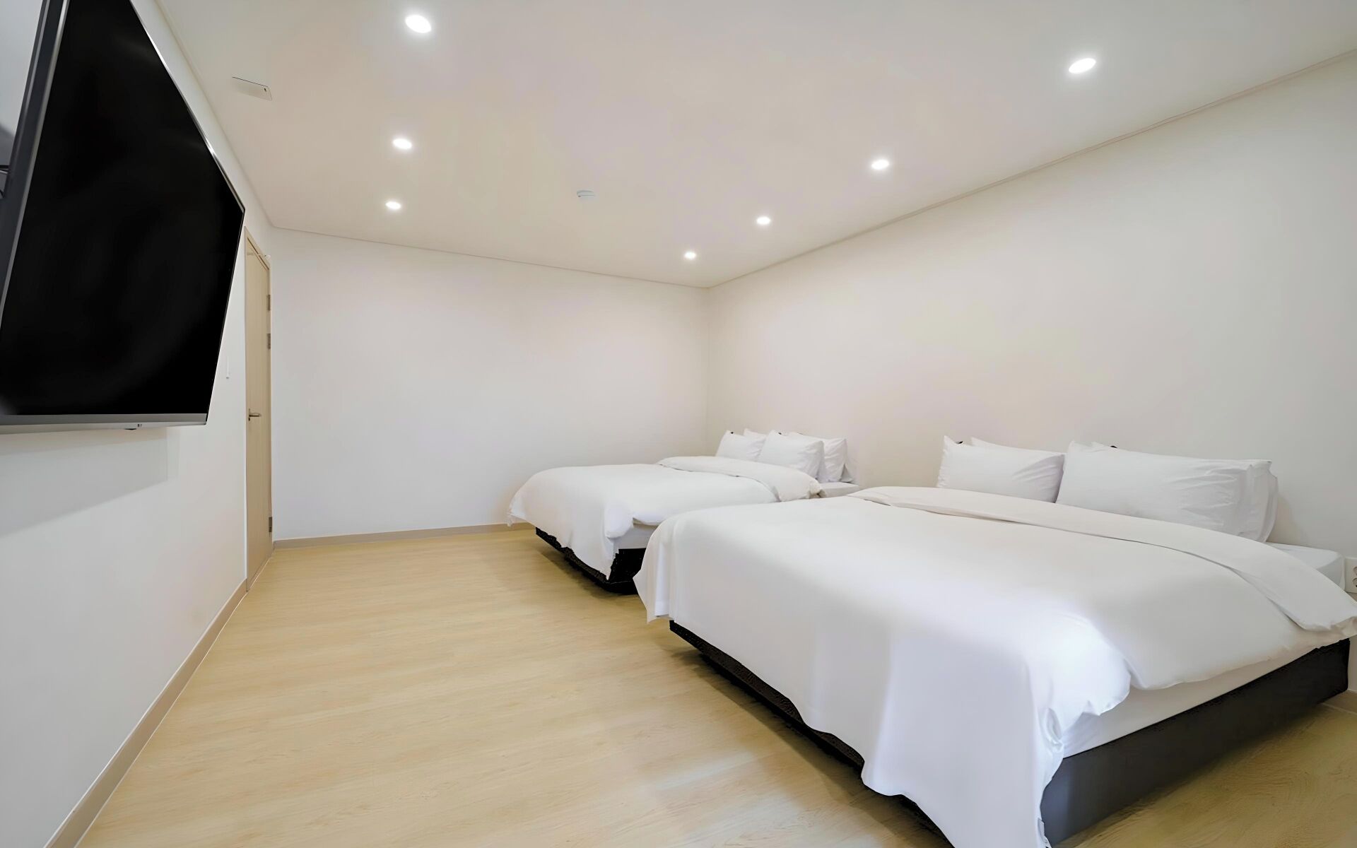 Habitación de hotel con dos camas, un televisor de pantalla plana montado en la pared e iluminación empotrada en el techo.