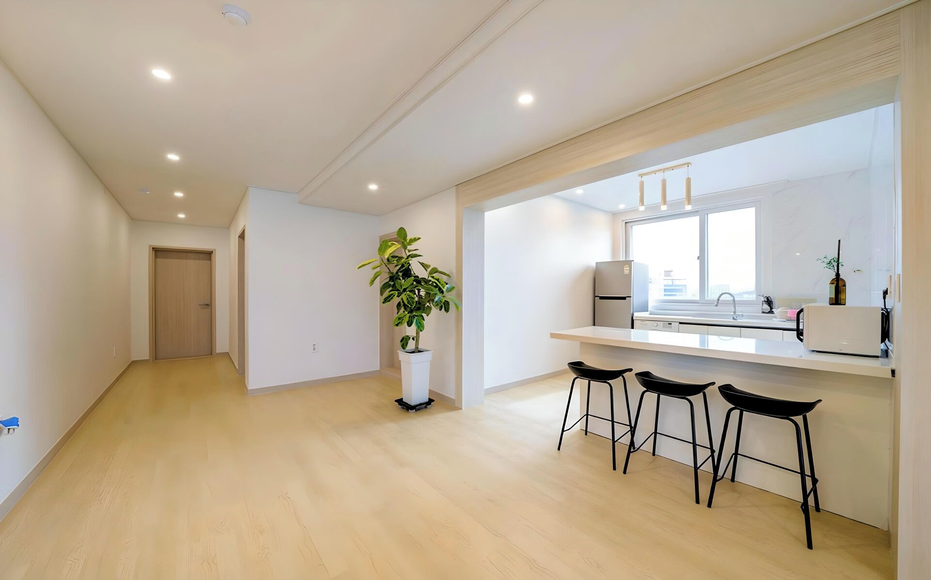 A modern kitchen with a large window, a refrigerator, and three black bar stools.
