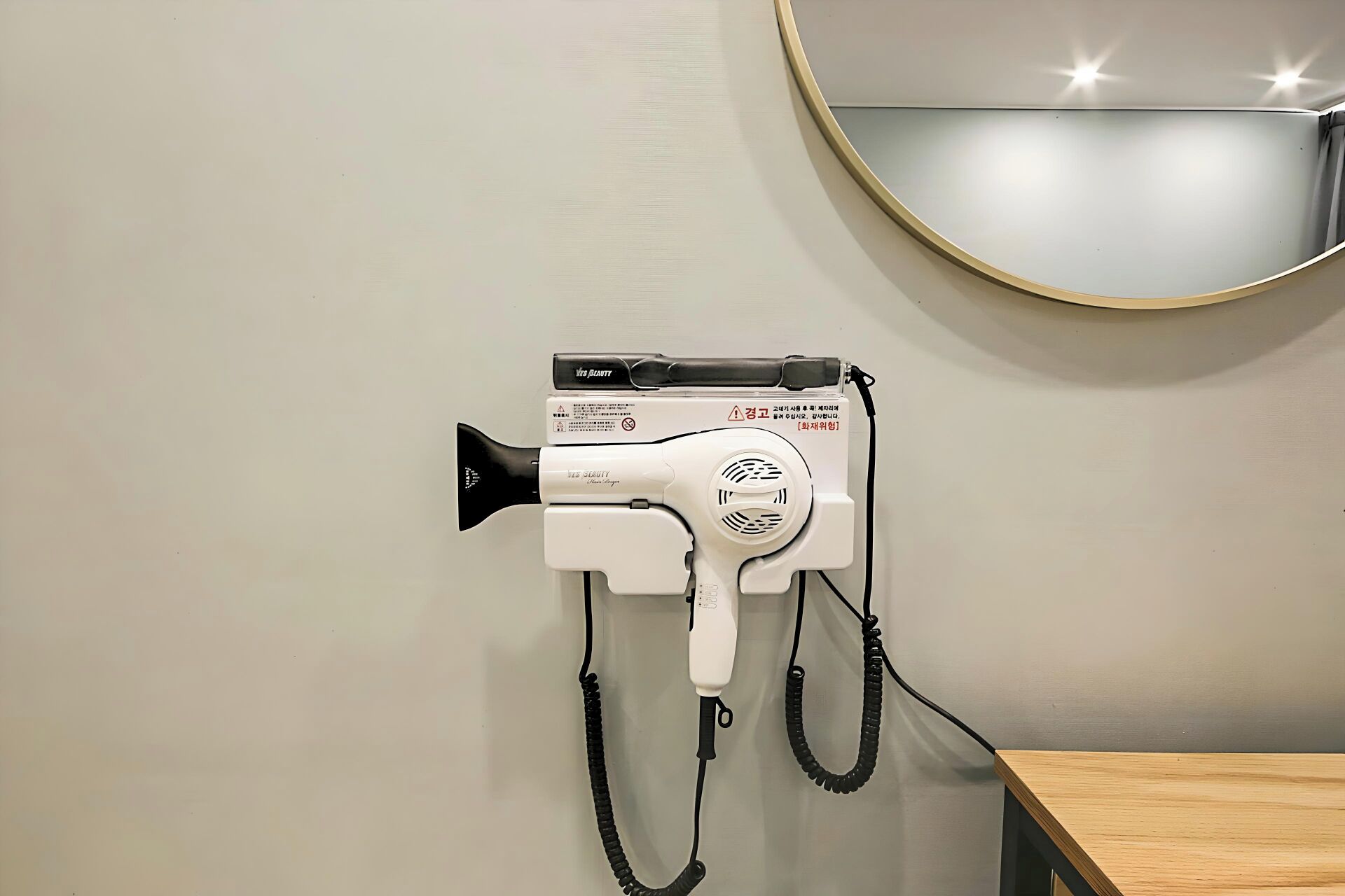 Un secador de pelo sujeto a la pared, con un espejo redondo encima.