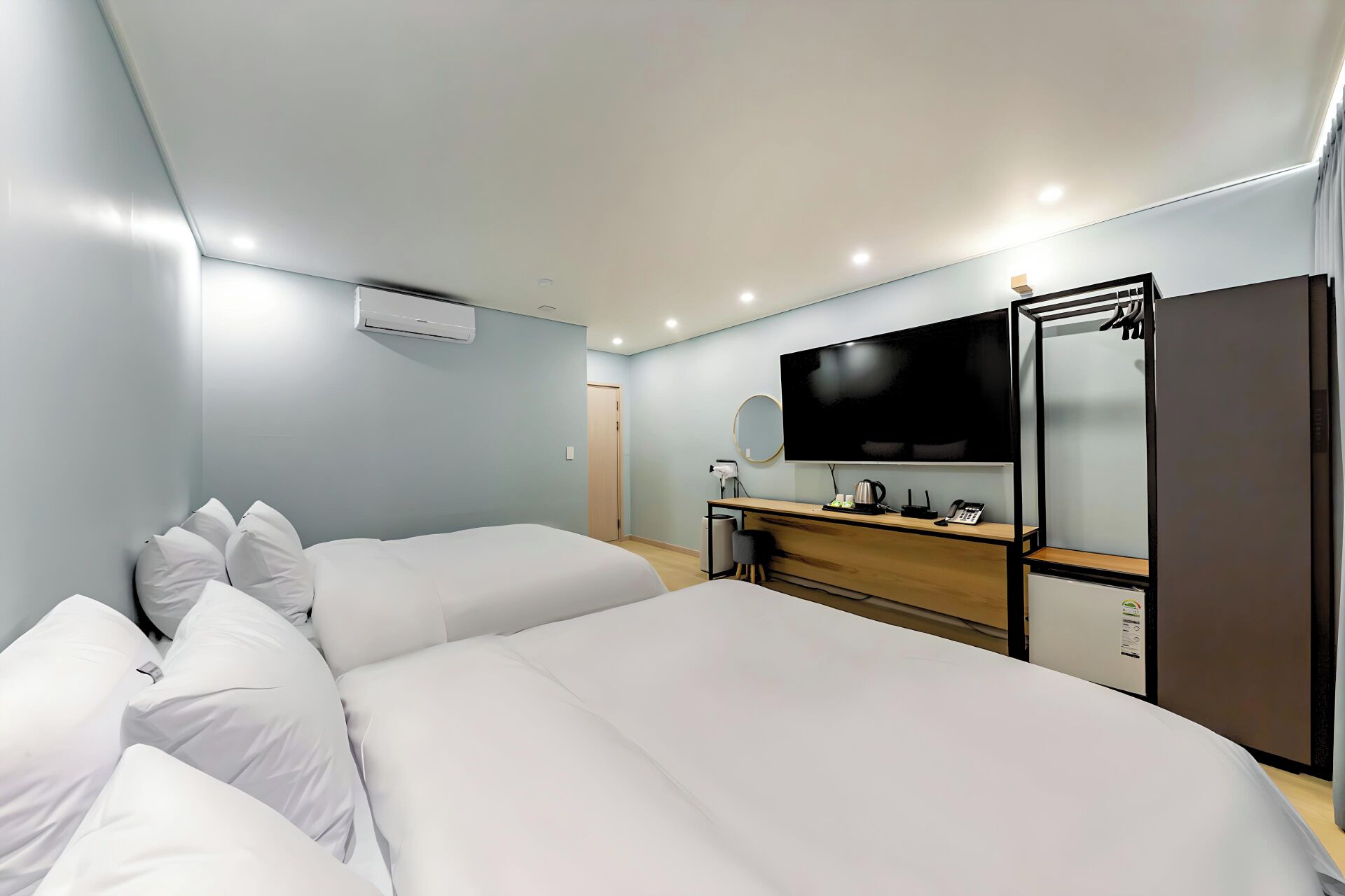 A hotel room with two beds, a desk with a flat-screen TV, a mirror, and a wardrobe.