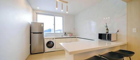 A modern kitchen with a built-in washing machine, a refrigerator, a microwave, and a bar area with stools.