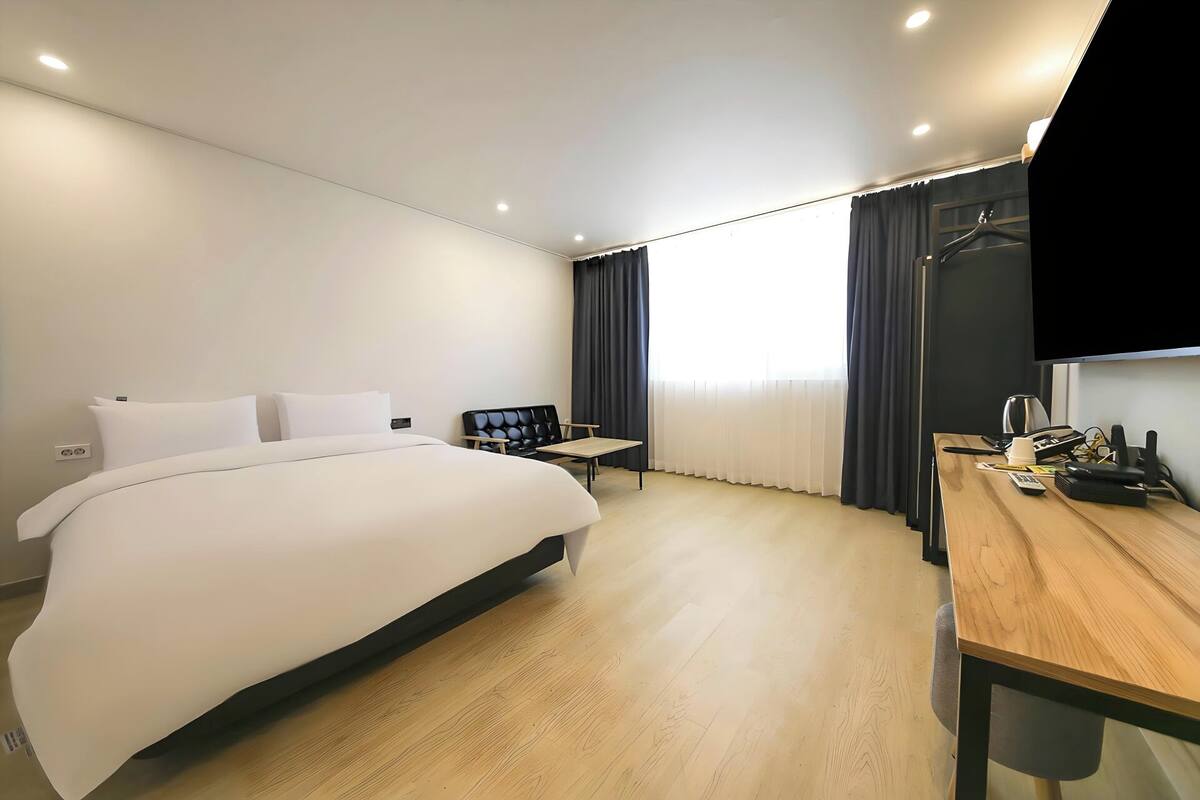 A hotel room with a bed, a desk, a chair, a TV, and a window with curtains.