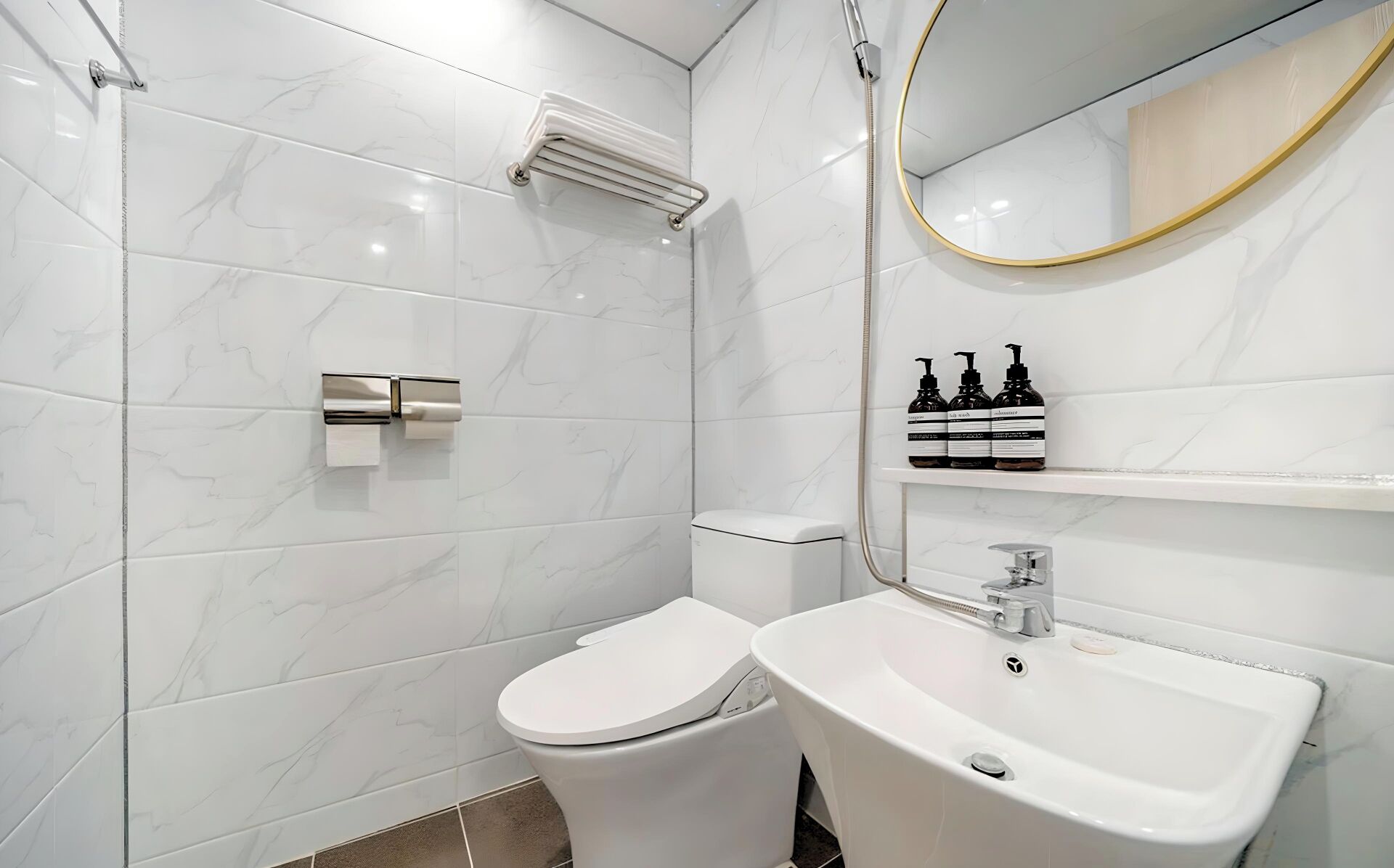 Une salle de bain moderne avec des toilettes, un lavabo et une douche. On trouve des articles de toilette sur une étagère.