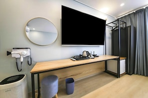 A modern hotel room with a large flat-screen TV, a round mirror, a desk with a kettle, a hairdryer, and a trash bin. - Ayana Hotel & Resort (Mokpo)