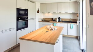 Moderni keittiö, jossa on valkoiset kaapit, puinen työtaso ja kahvinvalmistusalue.