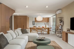 A modern living room with a sectional sofa, a dining area with a wooden table and chairs, and a kitchen in the background. - Nareo Villa Collection - Villa Eora, Labin, Croatia (Labin)