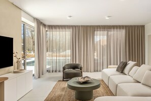 Ein modernes Wohnzimmer mit einer Couch, einem runden Couchtisch, einem Fernseher und einem Sessel.