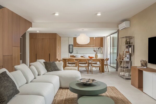 A modern living room with a sectional sofa, a dining area with a wooden table and chairs, and a kitchen in the background. - Nareo Villa Collection - Villa Nara, Labin, Croatia (Labin)