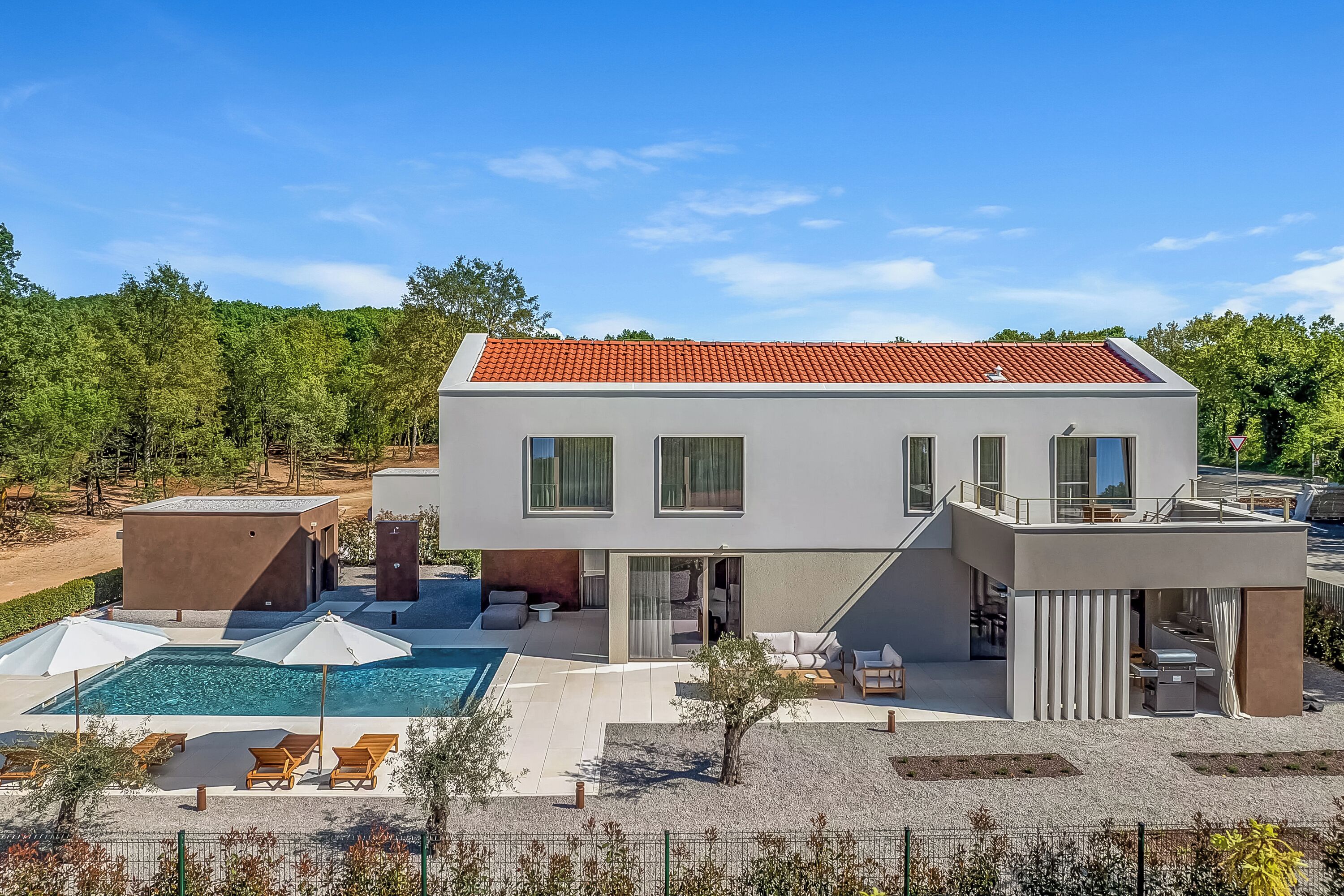 Ein modernes, zweistöckiges Haus mit Swimmingpool, Sitzgelegenheiten im Freien und einer überdachten Terrasse.