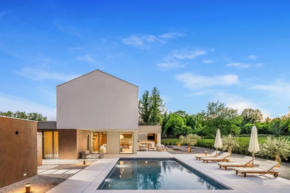 Ein modernes Haus mit Swimmingpool, Sitzgelegenheit im Freien und einem gepflegten Garten.