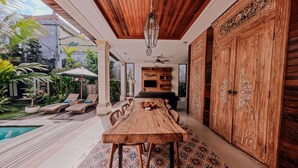 Una mesa de comedor de madera con sillas, un ventilador de techo y una piscina al fondo.
