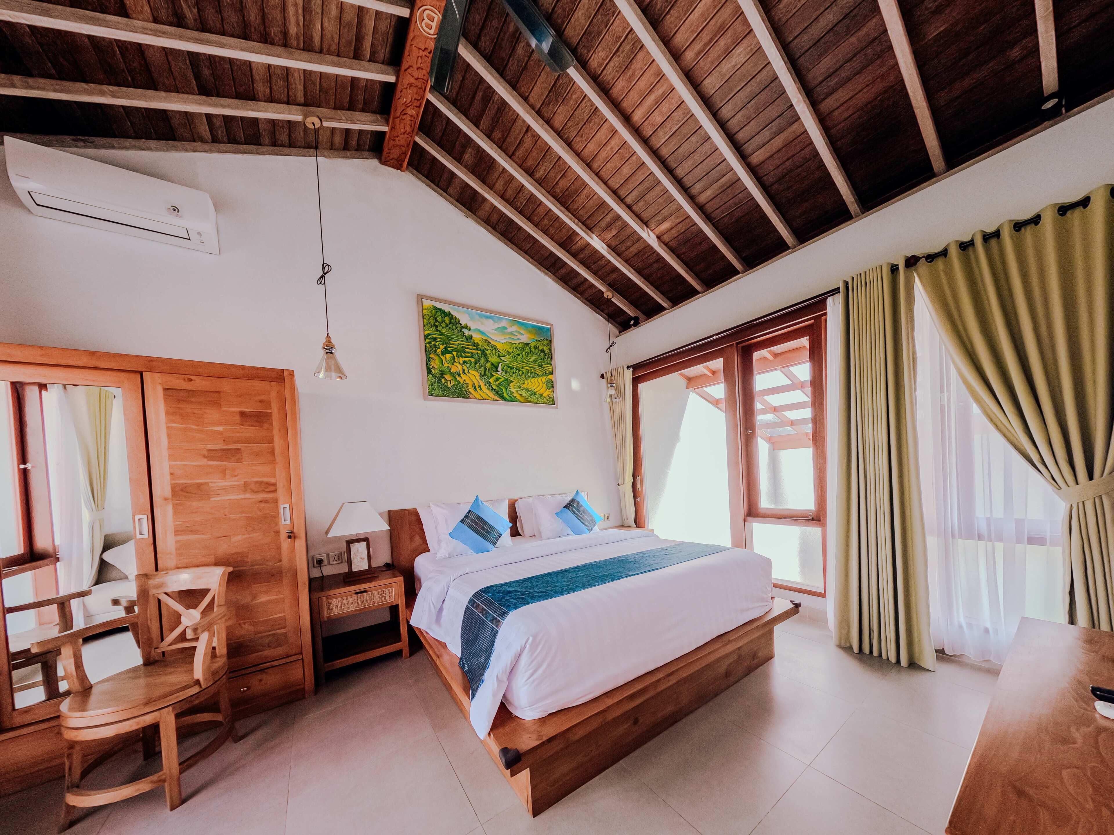 A bedroom with a wooden bed, a desk with a chair, a nightstand, a painting, and a large window with curtains.