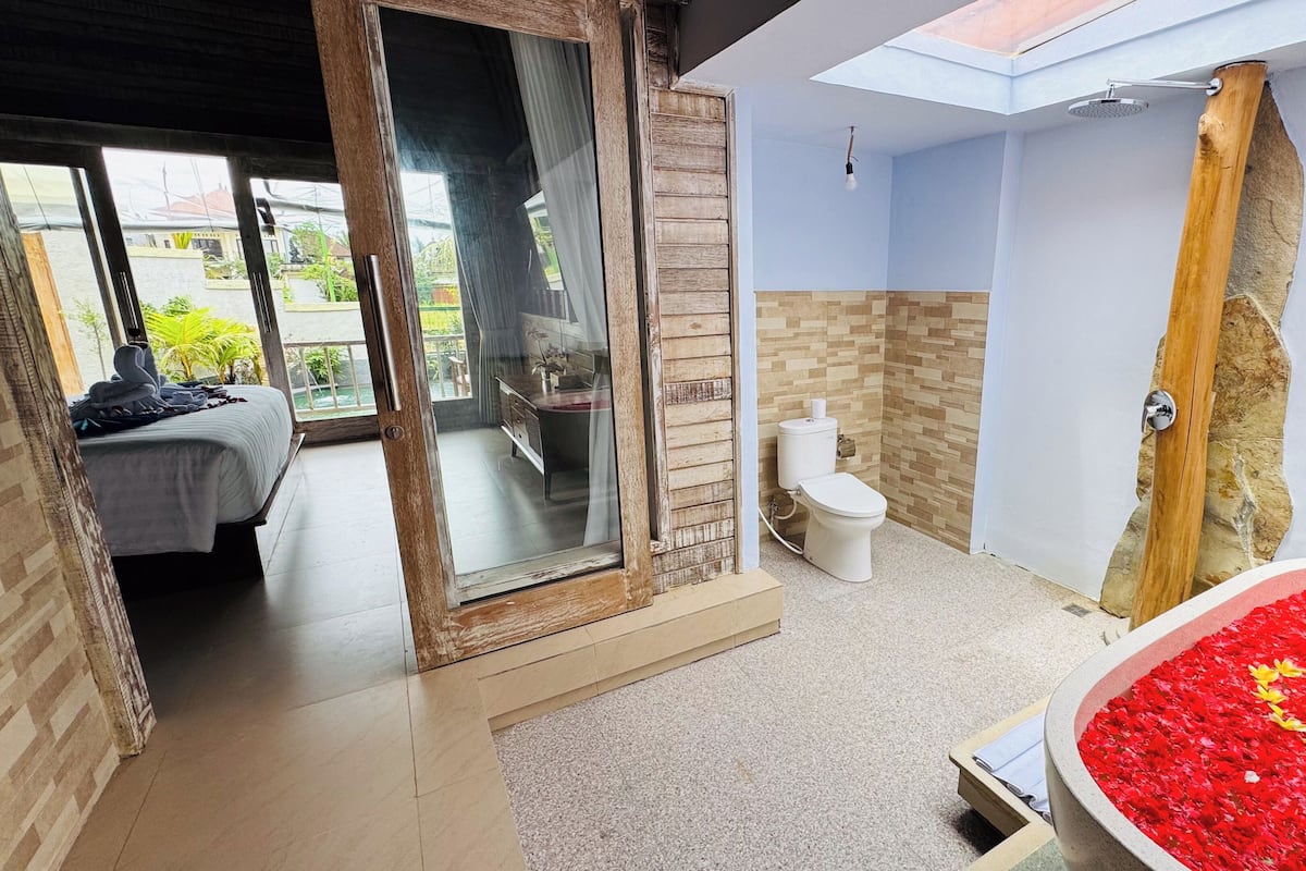 Ein Badezimmer mit Dusche, Toilette und einer großen Badewanne voller Rosenblätter.