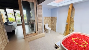 A bathroom with a shower, toilet, and a large bathtub filled with rose petals. - Bonito Suite Villa (Ubud)