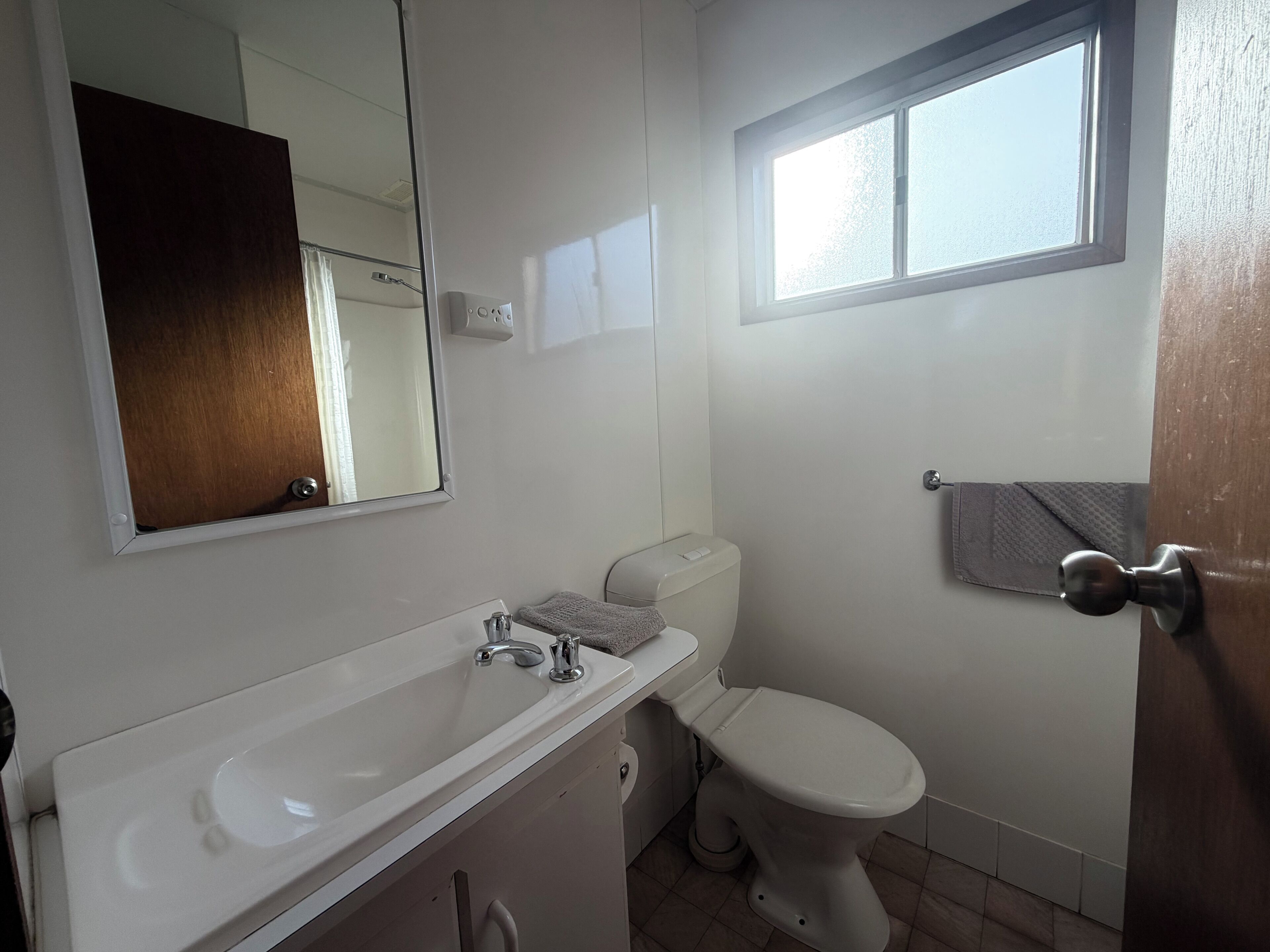 A bathroom with a white sink, a toilet, a mirror, and a window.