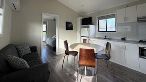 A modern kitchen with white cabinets, a dining table with chairs, a ceiling fan, and a TV on the wall. - Tiny Away Escape at Talbingo Alpine (Talbingo)