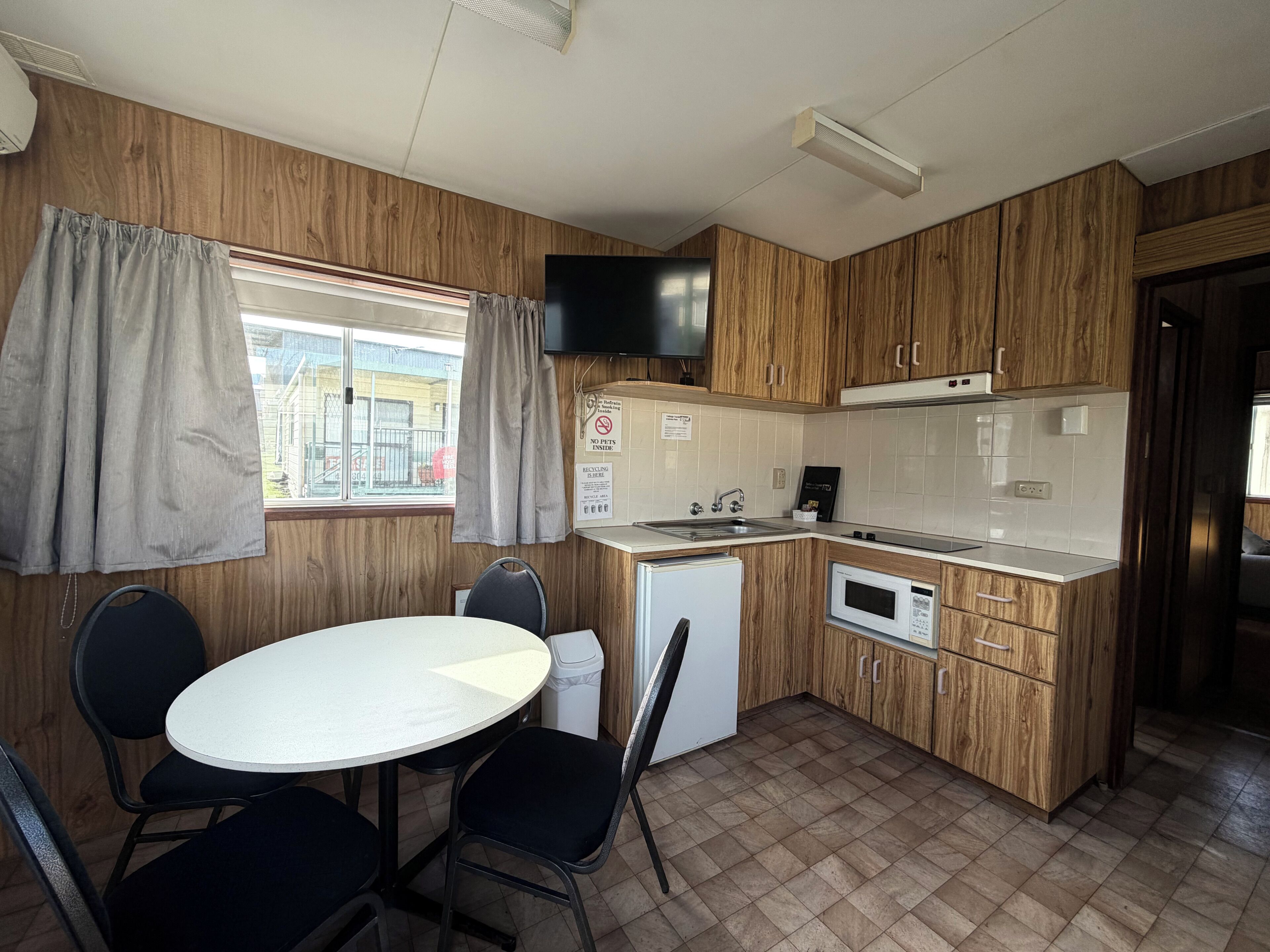 A compact kitchen with a dining area, wooden cabinets, a small refrigerator, and a flat-screen TV.