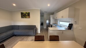 A modern living space with a sofa, dining table, kitchen area, and a painting on the wall. - Tiny Away Escape at Talbingo Alpine (Talbingo)