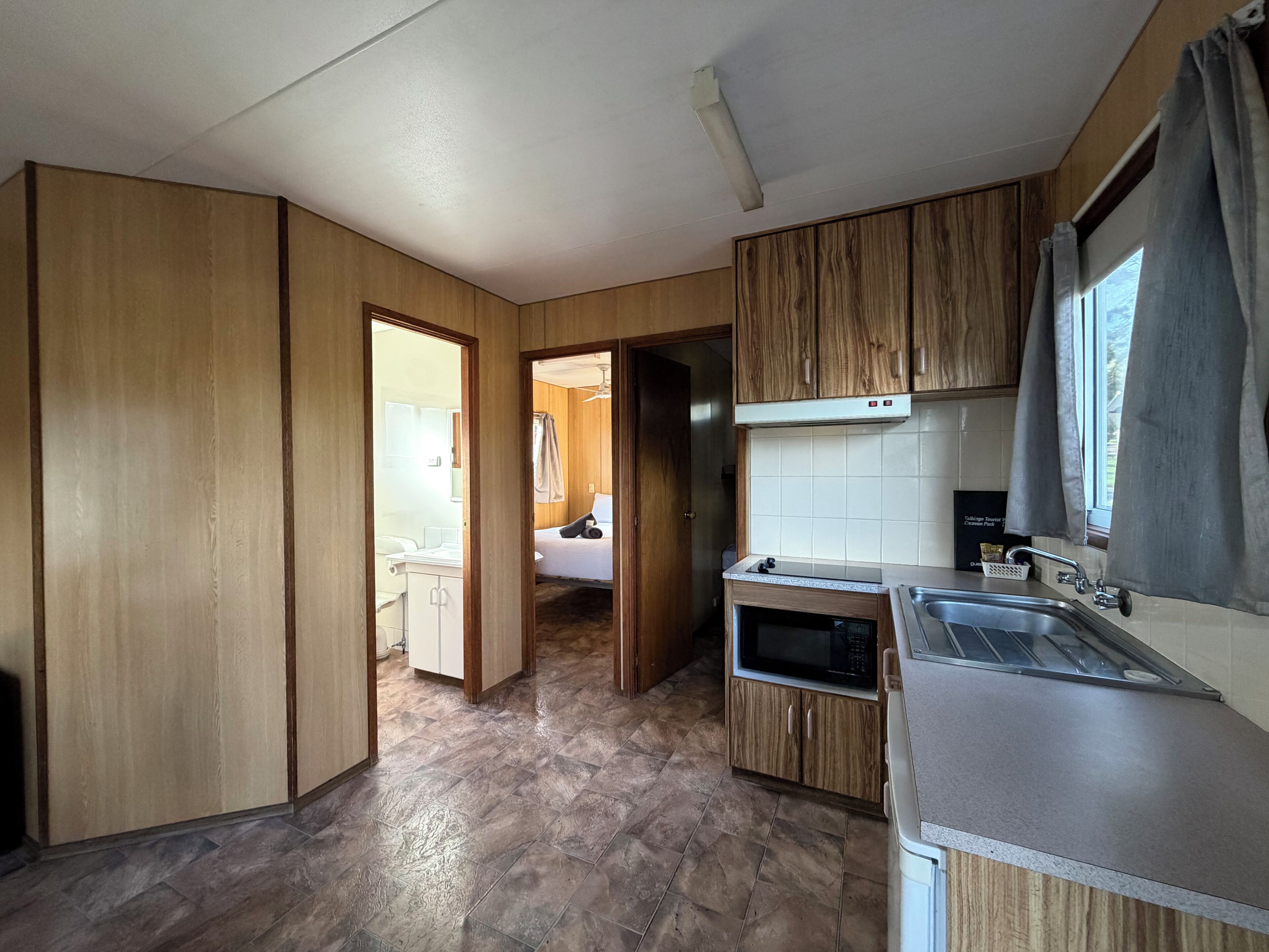 Cocina compacta con armarios de madera, microondas y lavamanos.