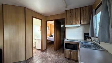 Cocina compacta con armarios de madera, microondas y lavamanos.