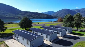 A row of modern, single-story buildings with flat roofs, likely part of a hotel or resort, situated in a scenic area with a lake and mountains in the background. - Tiny Away Escape at Talbingo Alpine (Talbingo)
