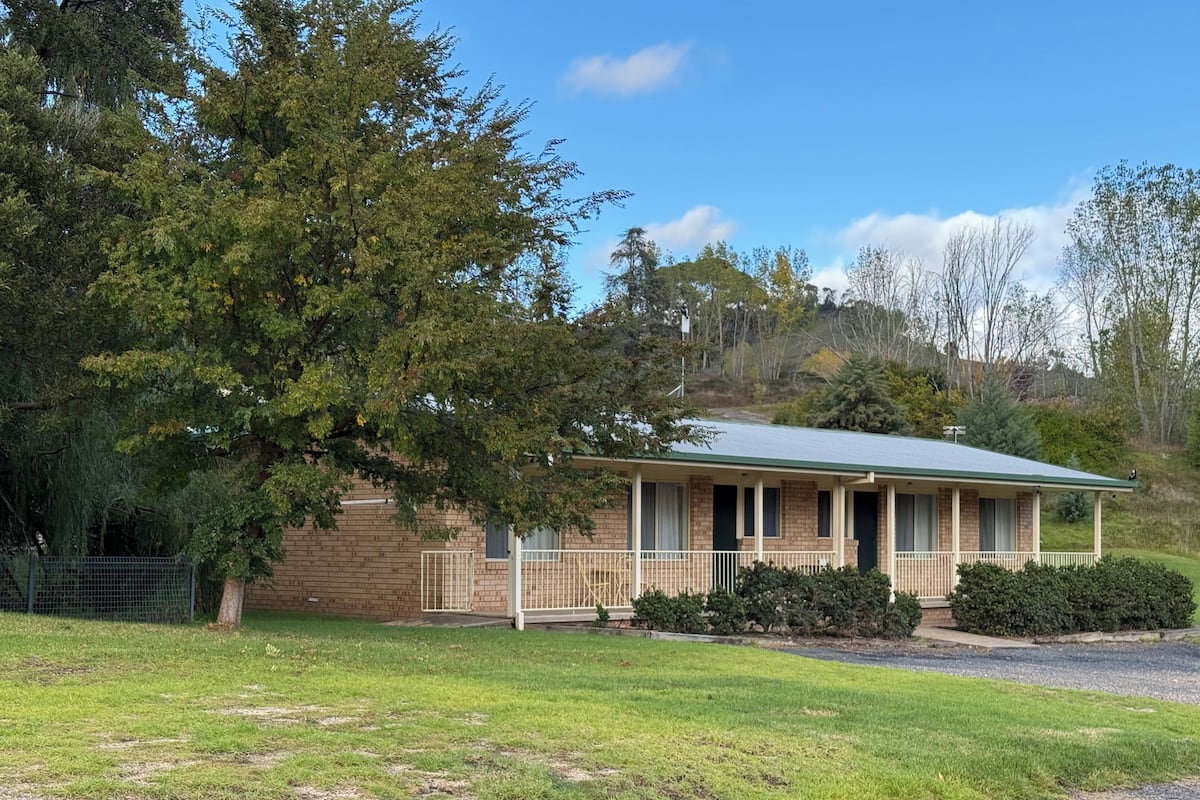A single-story brick house with a green roof, a covered porch, and a fenced yard.